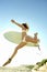 Young surfer jumping onto beach with board under arm