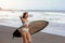 Young surfer woman in bikini going surfing stands with surfboard on the black sandy beach. Girl walks with longboard