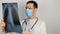 A young surgeon wearing a protective medical mask examines an X-ray of a patient's lungs and ponders the diagnosis.