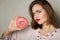 Young suspecting model with natural makeup holding glaze donut over a grey background. Space for text