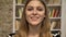 Young sweet blonda is watching at camera, smiling, library on background