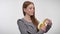 Young sweet ginger girl is peeling banana, biting it, enjoying, white background