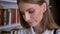 Young sweet girl is watching in book, watching at camera, library on background