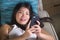 Young sweet happy and pretty Asian Korean girl using internet social media app on mobile phone smiling cheerful lying on home sofa
