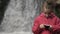 Young sweety five-year-old girl using smart phone while standing in front of waterfalls in beautiful nature