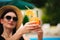 Young tan model in stylish summer outfit enjoying pool party , holding tasty alcohol cocktail .