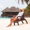 Young tanned woman sit at the chair and relax near bungalow of resort on the beach. Happy woman vacation. Island lifestyle. Rest