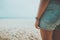 Young tanned woman standing relax on a tropical beach. Blue sea in the background.