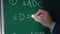 Young teacher man writes mathematical formulas using chalk on a green school chalkboard