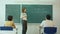 Young teacher near chalkboard in school classroom talking to class