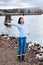 Young teen girl with arms lifted and outstretched, praising God on rocky shore by lake