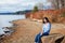 Young teen girl in blue shirt and jeans sitting along rocky lake shore