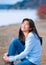 Young teen girl in blue shirt and jeans sitting along rocky lake shore