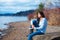 Young teen girl in blue shirt and jeans sitting along rocky lake shore