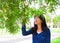 Young teen girl outdoors, reaching up to touch leaves on tree