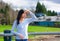 Young teen girl standing, leaning against railing at park shading eyes to look off to side