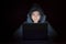 Young teen woman wearing hood on looking dark and hacking laptop