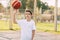 A young teenage basketball player in a white t-shirt stands on the basketball court, twirling a basketball on his