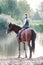 Young teenage girl riding horseback to river at early morning