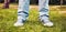 Young teenager foot and legs with blue sneakers and jeans on the green grasses of a garden. Youth fashion