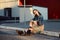 Young teenager girl sitting on the road outside near urban red wall background in skirt and jeans jacket on the sunset.