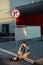 Young teenager girl sitting on the road outside near urban red wall background in skirt and jeans jacket on the sunset.