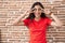 Young teenager girl standing over bricks wall doing peace symbol with fingers over face, smiling cheerful showing victory