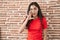 Young teenager girl standing over bricks wall hand on mouth telling secret rumor, whispering malicious talk conversation