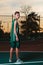 A young teenager in a green tracksuit poses with a basketball on a sports field. Back view. Sunset in the background. Concept of