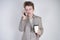 Young teenager with surprised emotions in grey business clothes standing with mobile phone and paper cup of coffee on white studio