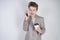 Young teenager with surprised emotions in grey business clothes standing with mobile phone and paper cup of coffee on white studio