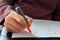 Young teenager using an orange color highlighter pen to drawing flower and sun cartoon icon on the paper in the classroom.