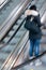 Young teenager woman in movement standing alone in an urban up moving escalator leaving  the subway station traveling upstairs