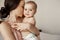 Young tender happy mother hugging her newborn baby smiling sitting on bed in morning.