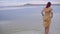 Young thin girl in yellow striped dress comes into water of salt lake in shoes