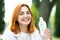 Young thirsty redhead woman drinking water from a bottle in summer park