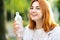 Young thirsty redhead woman drinking water from a bottle in summer park