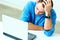 Young thoughtful businessman in blue shirt sitting at the table with laptop