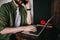 Young thoughtful man watching webinar at laptop and typing ideas for coursework text