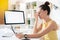 Young tired businesswoman in dress sitting by desk in front of computer monitor