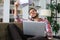 Young tired freelancer in casualwear sitting on sofa in front of laptop