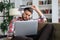 Young tired freelancer in casualwear sitting on sofa in front of laptop