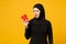 Young tired sad upset arabian muslim woman in hijab black clothes hold paper cup of coffee isolated on yellow wall