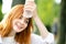 Young tired smiling redhead woman drinking water from a bottle in summer park