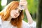 Young tired thirsty redhead woman drinking water from a bottle in summer park