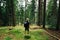 Young tourist in casual clothes stands on the moss in the woods on a climb up the mountain with a backpack on his back and looks