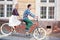 Young tourist couple, handsome man and pretty blond woman riding tandem bicycle along city street.