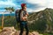 A young tourist girl with a backpack enjoys the sunset from the top of the mountain. Portrait of a traveler in a red riding hood.