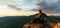 A young tourist girl with a backpack enjoys the sunset from the top of the mountain. A traveler on the background of mountains.