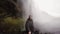 Young tourist man with selfie stick filming on gopro camera powerful waterfall Seljalandsfoss in Iceland in overcast day